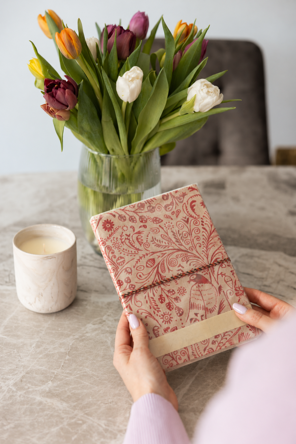 Crimson Peacock block print fabric diary held over a marble table beside a vase of tulips and a white candle