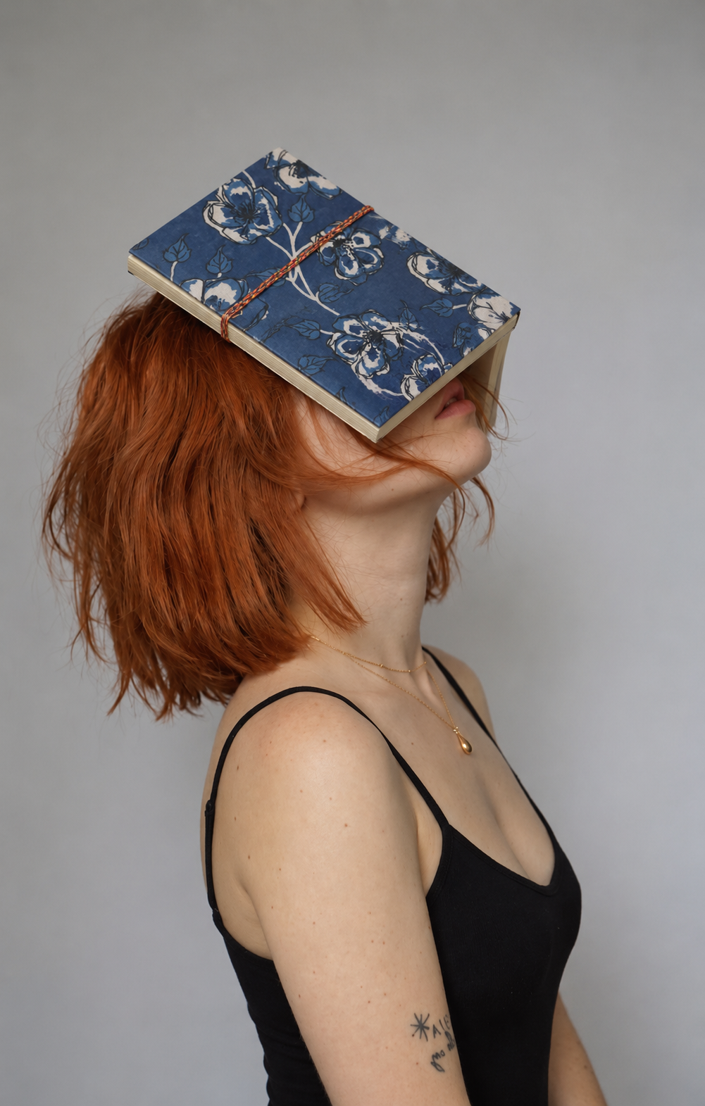 Cobalt blue block print fabric diary with large white-outlined flowers, resting open over the face of a woman in a black camisole