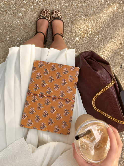 Amber Buti block print fabric diary on a white pleated skirt, seen from above with iced coffee and a burgundy chain bag