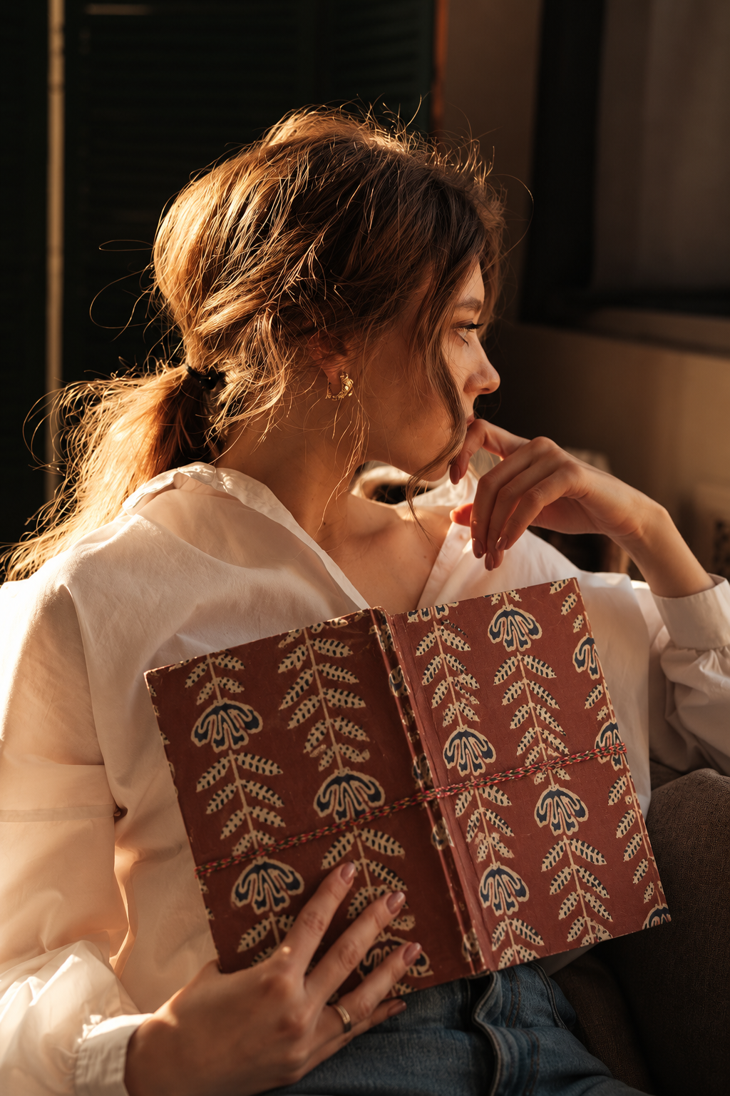 Crimson Jaipur block print fabric diary held open against a cream shirt, leaf-and-flower stems running across both covers