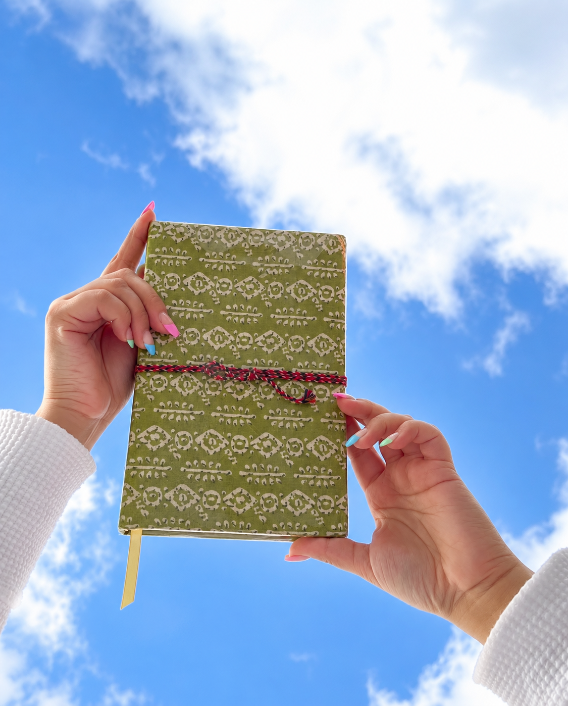 Mehendi Buti block print fabric diary held up against a blue sky with white clouds