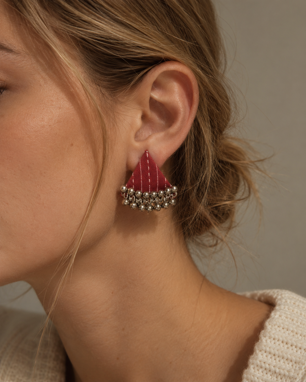 Riwaayat Pink Stitch triangle earrings with the hair pinned back: rani pink stitched fabric triangle above a ghungroo bell fringe