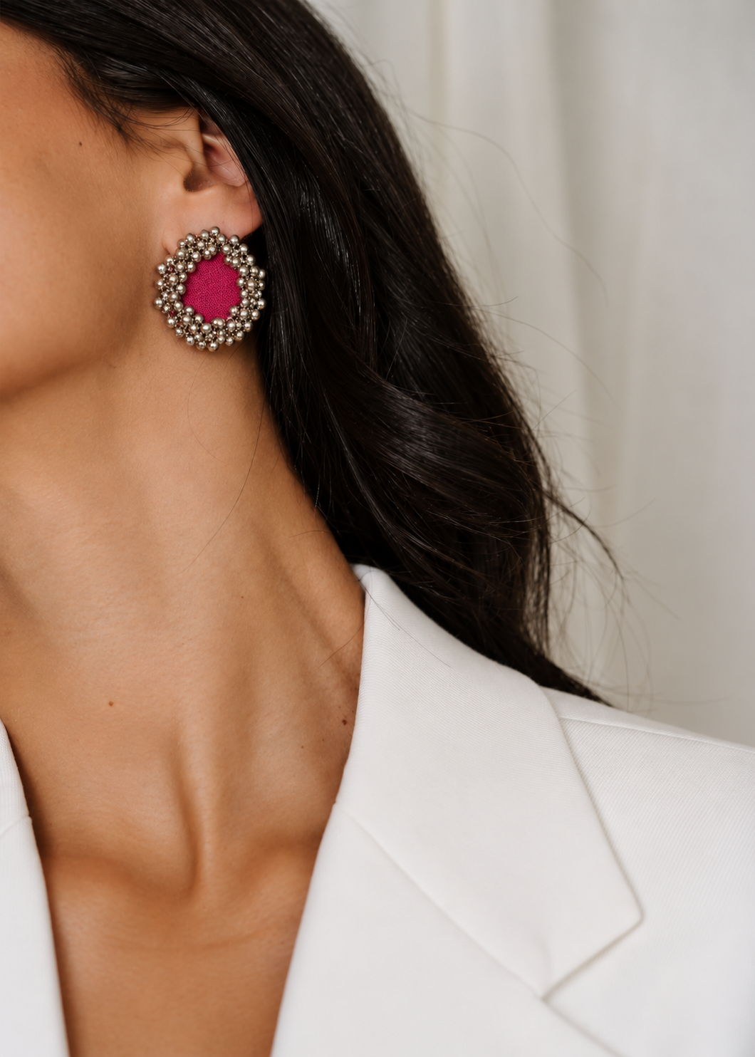 Fuchsia Pink Ghungroo Stud Earrings worn with a white blazer: fuchsia cotton centre ringed with two rows of silver-tone ghungroo bells