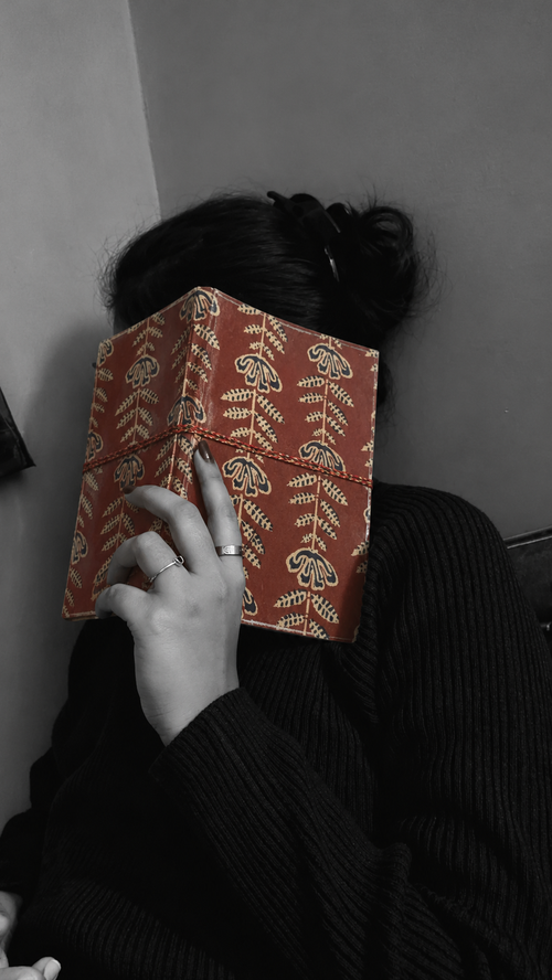 Crimson Jaipur block print fabric diary held over the face in a black and white portrait, the brick-red cover in colour