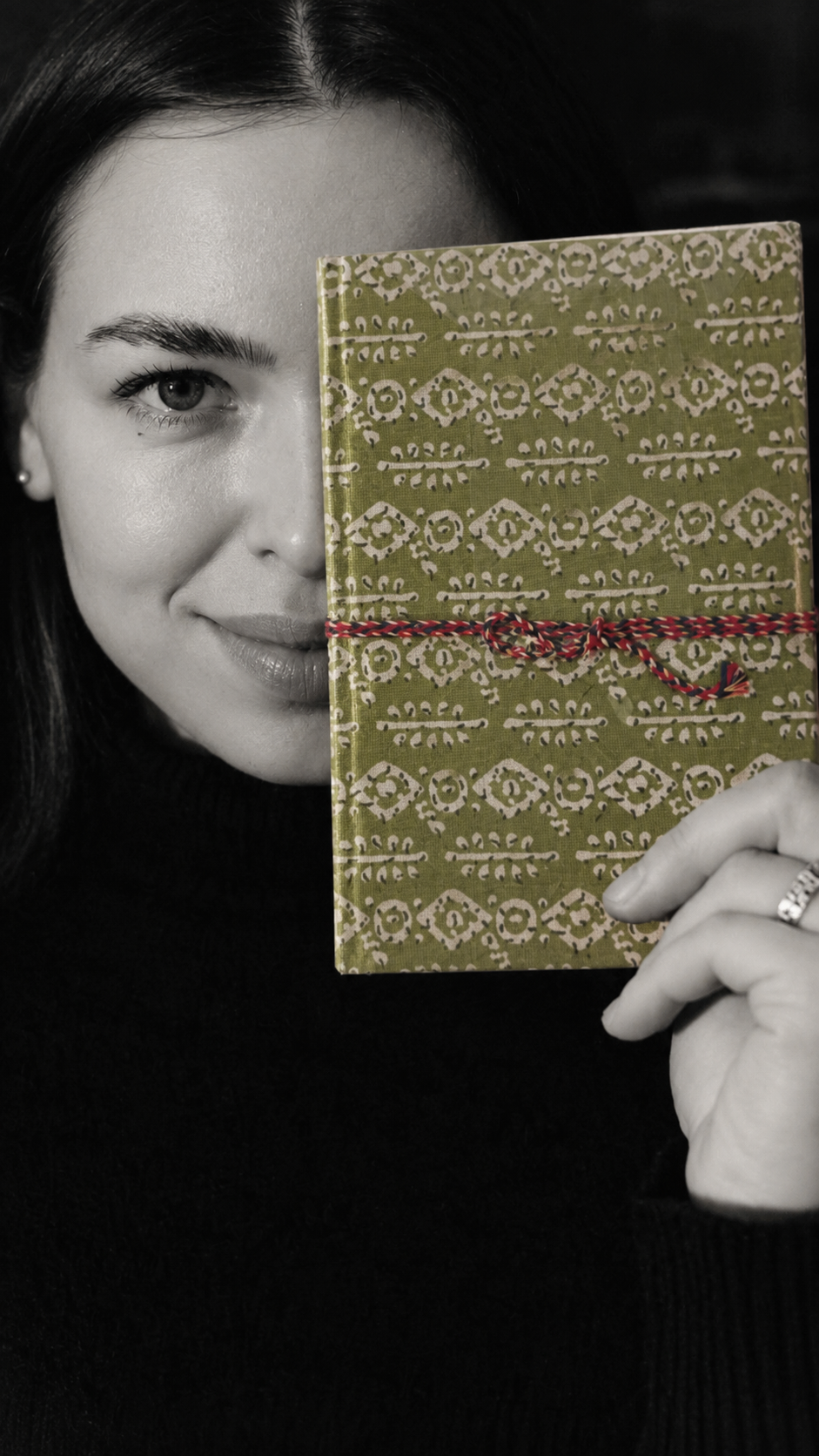 Mehendi Buti block print fabric diary held over half the face in a black and white portrait, the green cover in colour