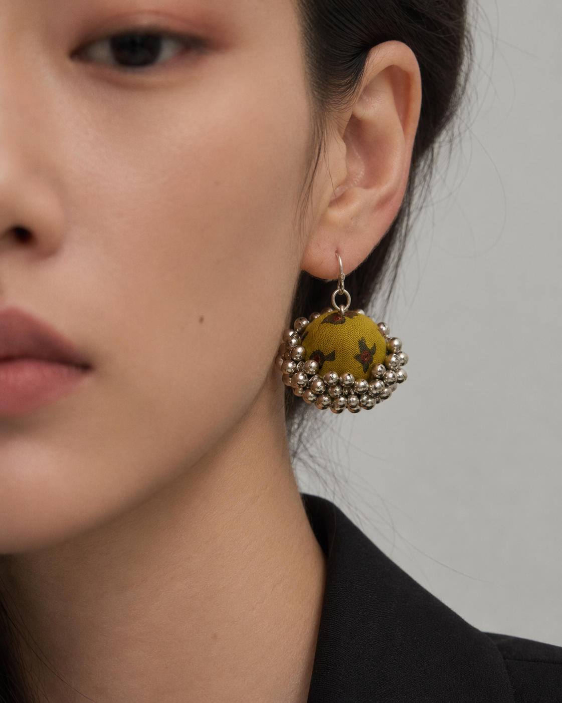 Mustard fabric jhumka earrings worn with a black jacket: mustard dome with small olive leaf motifs and a ghungroo bell fringe