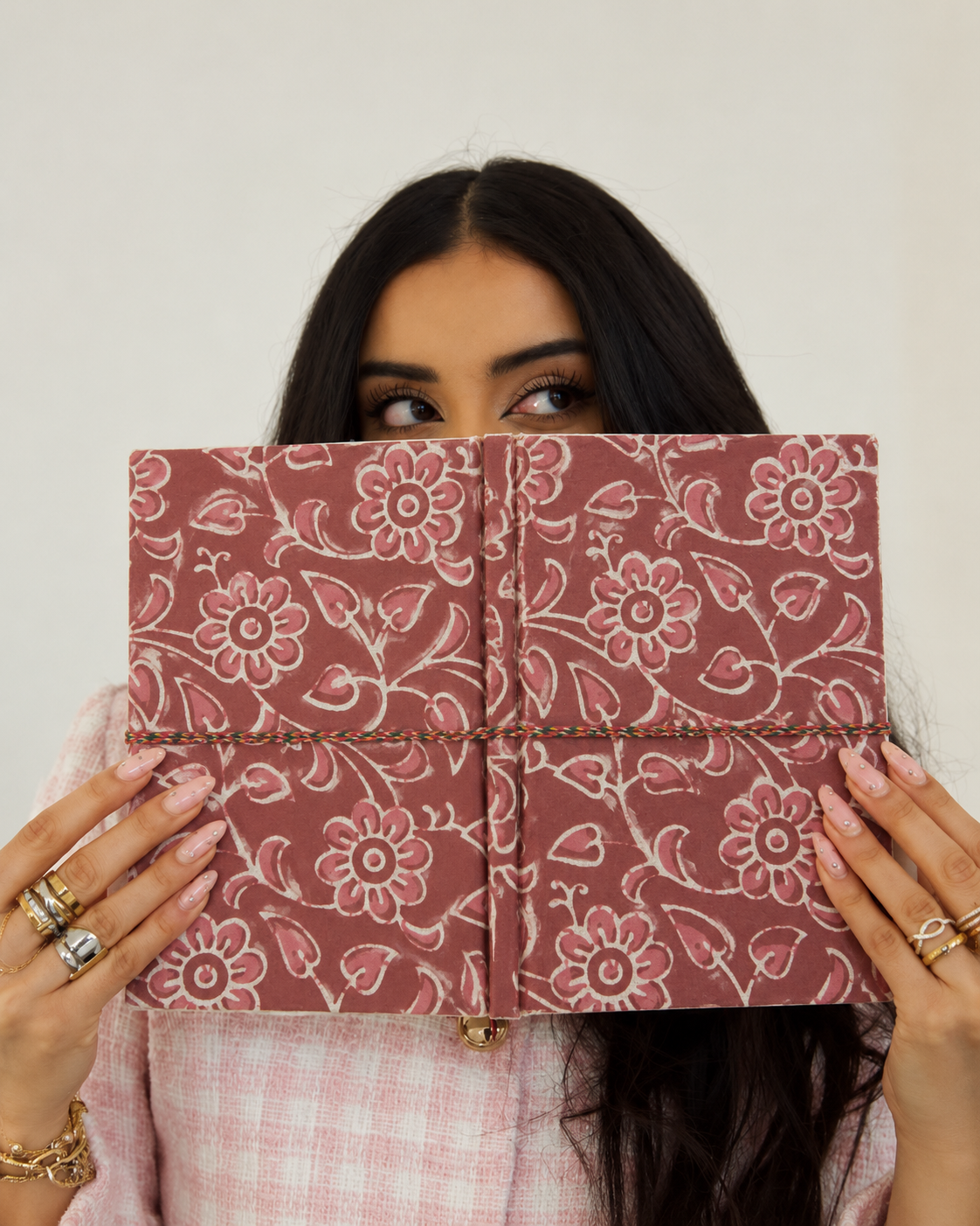 Block print fabric diary with outlined flowers and heart-shaped leaves, opened flat in front of the face, pink tweed jacket