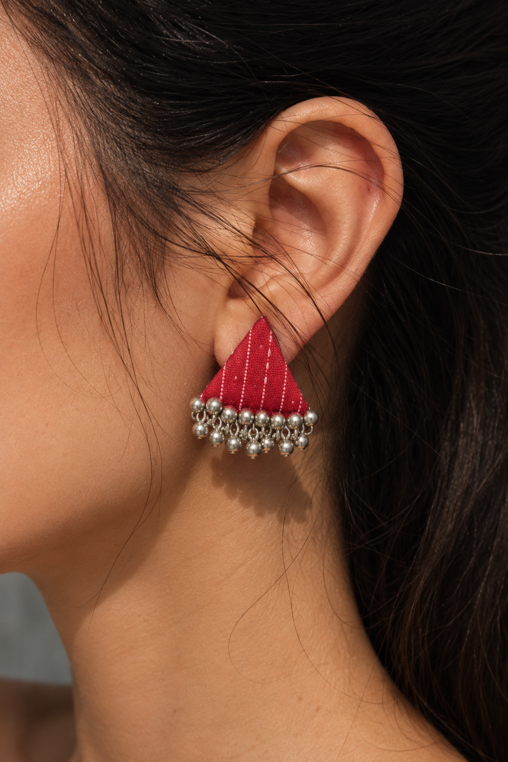 Close-up of a Riwaayat Pink Stitch triangle earring: white running stitches on rani pink fabric and antique-finish ghungroo bells