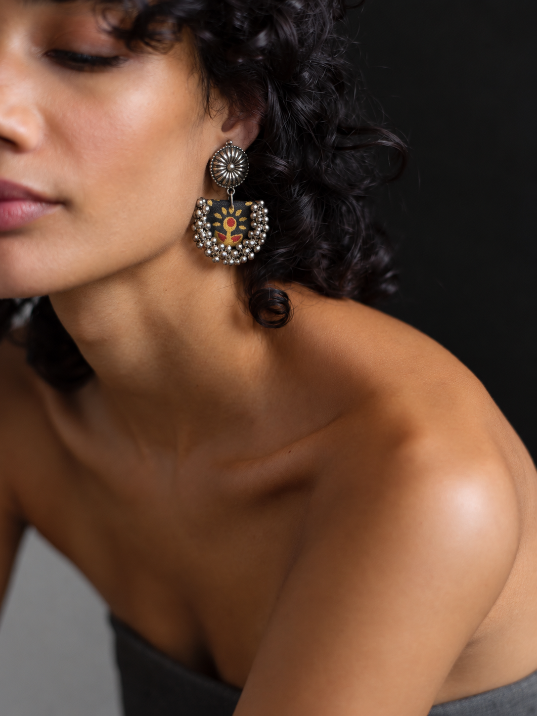 Black Chandbali Earrings with Ghungroo worn by a model with curly hair: black fabric crescent printed with mustard flowers, kundan top and ghungroo bells