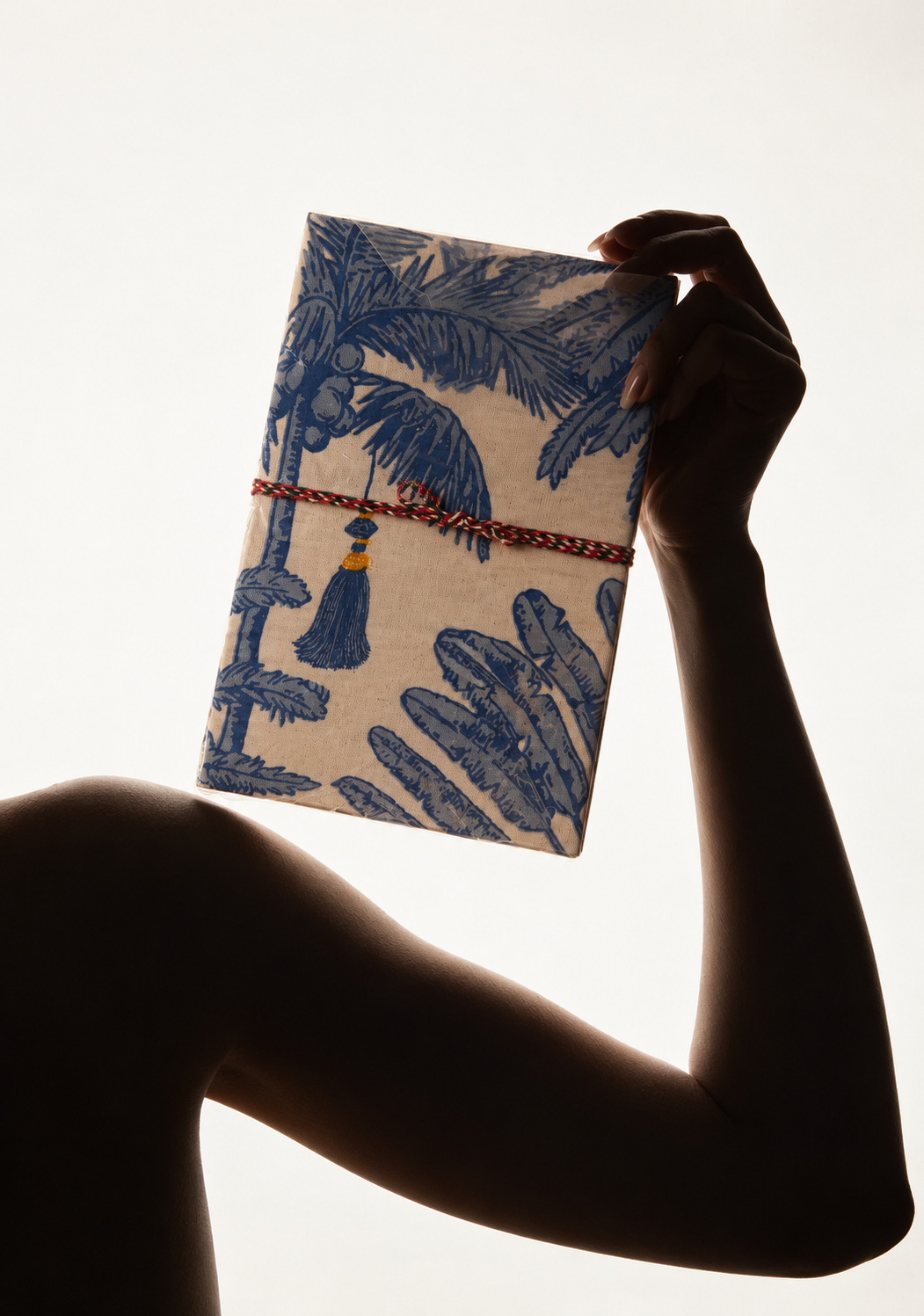 Neel Palash block print fabric diary held up by a silhouetted arm against bright light