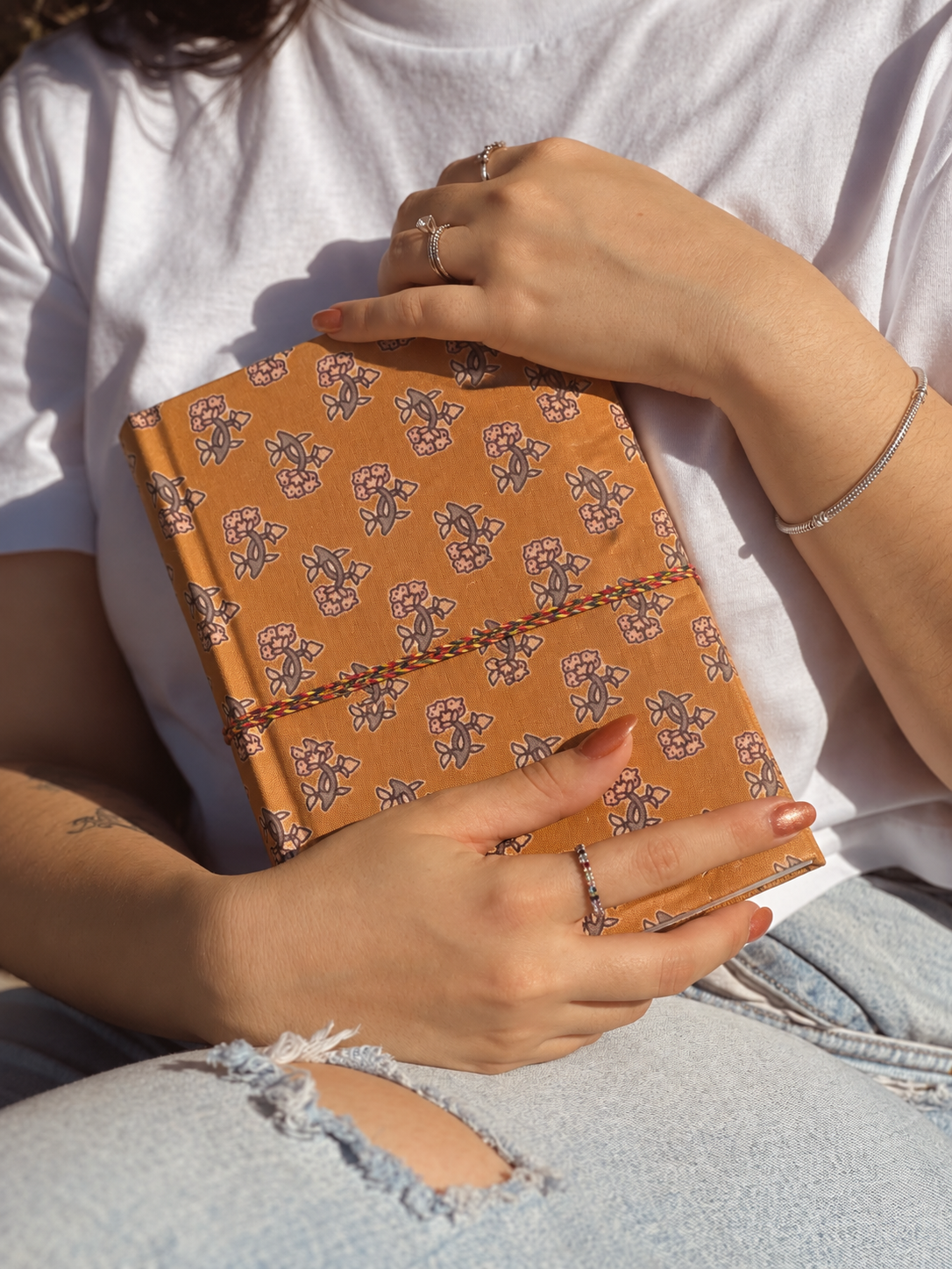 Amber Buti block print fabric diary held against a white T-shirt and ripped light blue jeans
