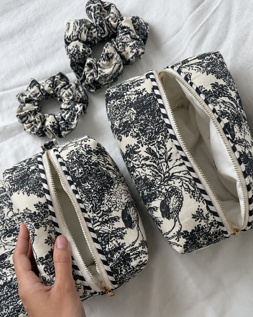 Two Angan quilted pouches in a black-and-white toile of trees and cranes, unzipped, styled with toile scrunchies (scrunchies not included)