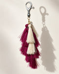 Aabha silk tassel bag charm: a small clear bead at the head, then long tiers of berry silk with ivory tassels set between them. It hangs from a silver-tone swivel clasp.