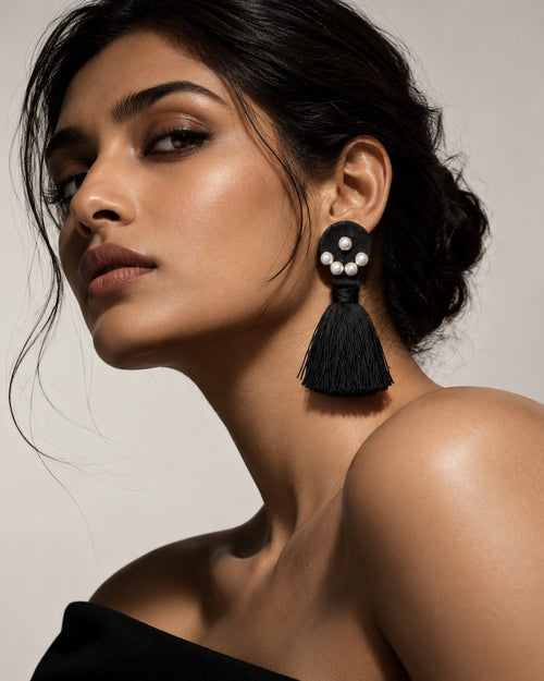 Black Tassel Earrings with Pearl Cluster worn on a model against a navy ground, pearl cluster and black tassel in profile (AI-generated styling image)