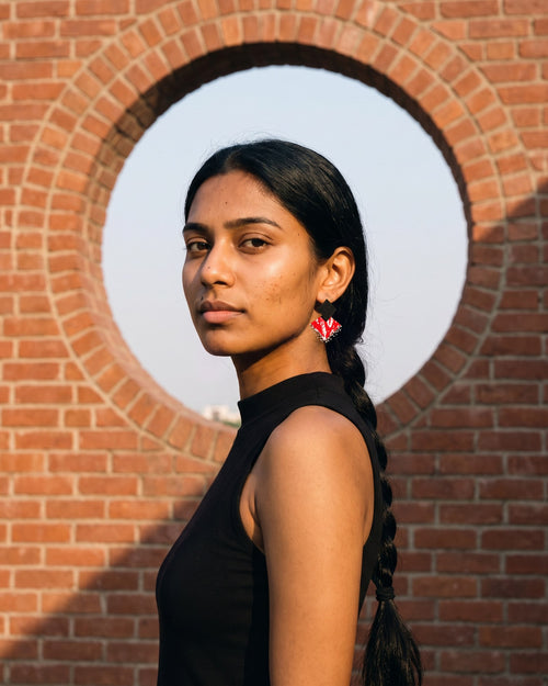 Black & Maroon Geometric Ghungroo Earrings worn with a black high-neck top in front of a round opening in a red brick wall (AI-generated styling image)