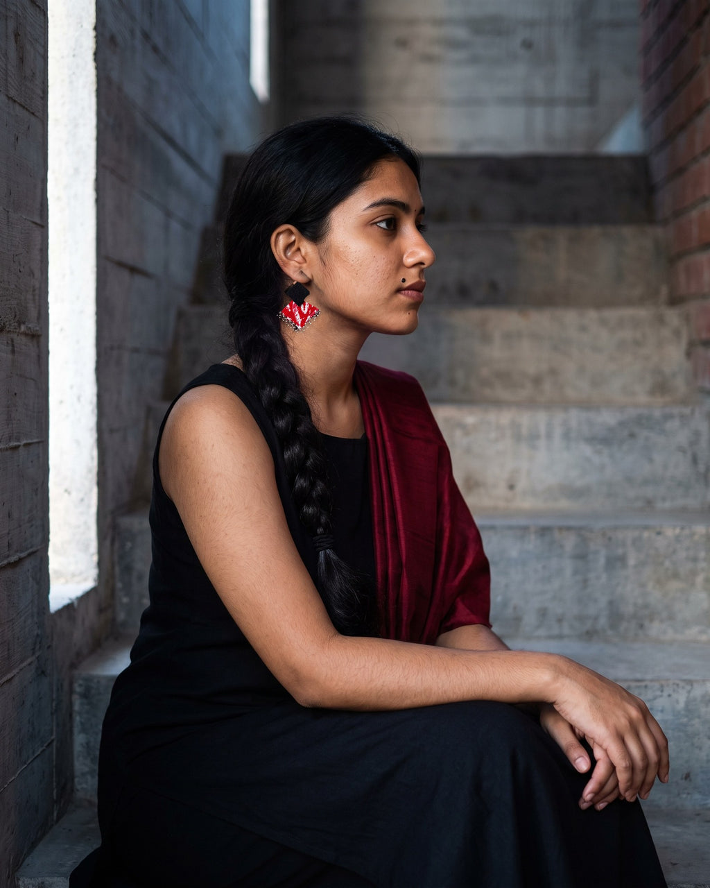 Black & Maroon Geometric Ghungroo Earrings worn with a black dress and a maroon stole on a concrete stair in evening light (AI-generated styling image)