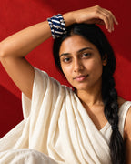 Lariya Navy Blue Leheriya Fabric Bangles with Ghungroo, Kada Set of 3, worn stacked on the wrist, arm raised over the head, ivory sari, red wall
