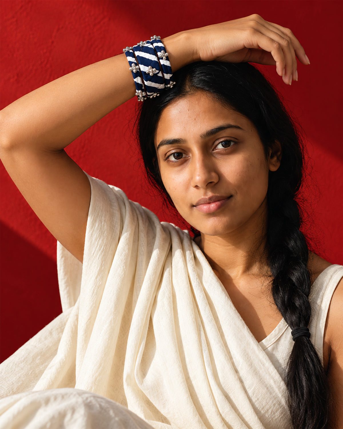 Lariya Navy Blue Leheriya Fabric Bangles with Ghungroo, Kada Set of 3, worn stacked on the wrist, arm raised over the head, ivory sari, red wall