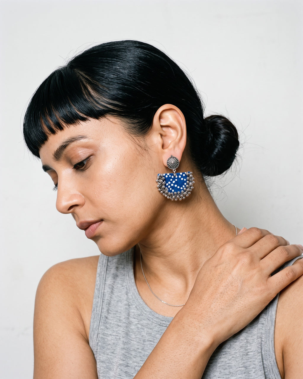 Blue chandbali earrings worn on a model in a grey vest, bone-white studio (AI-generated styling image)