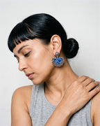Blue chandbali earrings worn on a model in a grey vest, bone-white studio (AI-generated styling image)