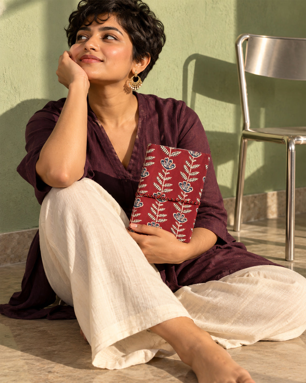 Crimson Jaipur Block Print Fabric Diary, 200 Unruled Pages, held on the knee, white outfit, green wall