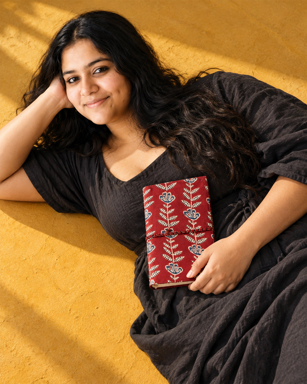 Crimson Jaipur Block Print Fabric Diary, 200 Unruled Pages, held at the chest, black dress, saffron yellow wall