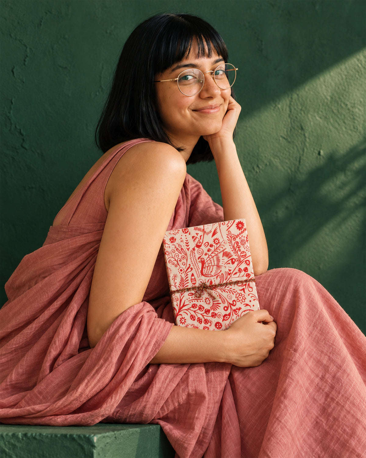 Crimson Peacock Block Print Fabric Diary, 200 Unruled Pages, held at the chest, pink dress, green wall