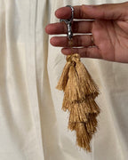 Zari silk tassel bag charm held in the hand to show its size, about 9 inches from clasp to fringe
