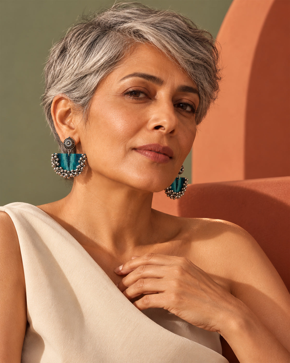 Teal Green Chandbali Earrings with Ghungroo worn by a silver-haired woman in an ivory one-shoulder top, olive and terracotta walls: teal striped fabric crescent with silver ghungroo bells