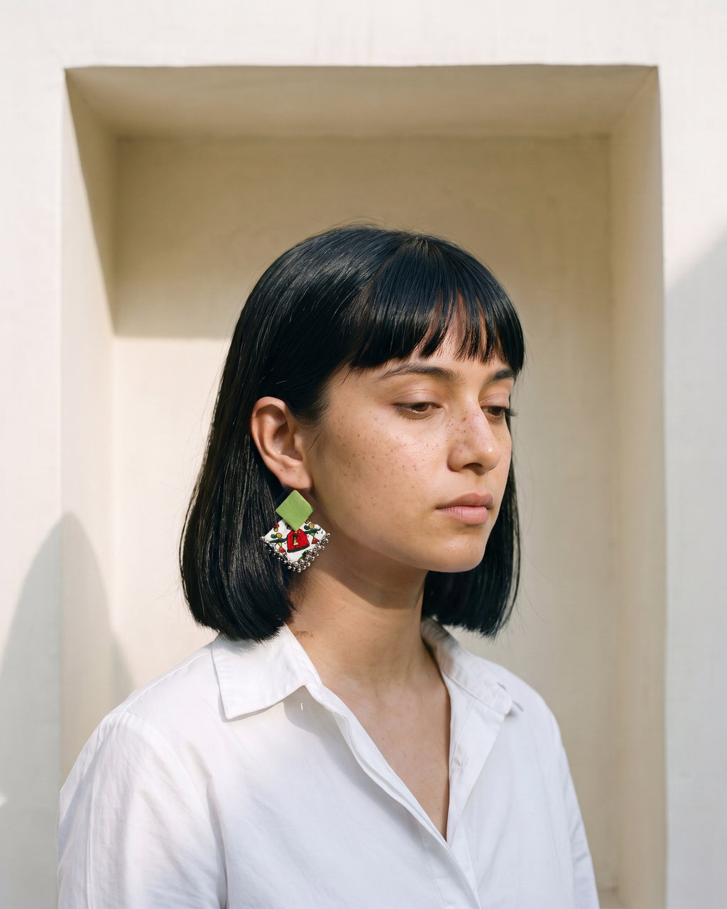 Teal Green Geometric Ghungroo Earrings worn with a white cotton shirt in an ivory lime-plaster niche (AI-generated styling image)