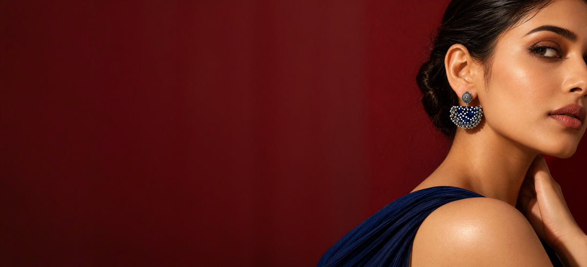 Model in a navy drape wearing the Blue Chandbali earrings, a fabric-covered base with kundan and ghungroo detail, against a crimson wall: handmade jewellery by House of Falguni
