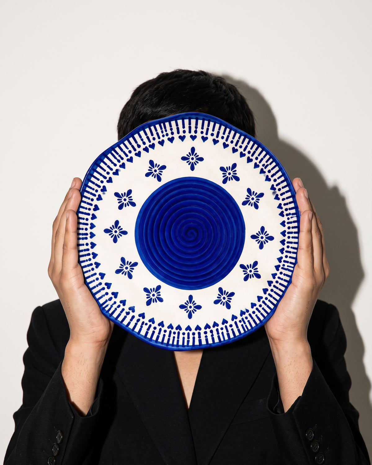 Heritage Blue Ceramic Quarter Plates (Set of 2) held up by a model in black, bone-white studio