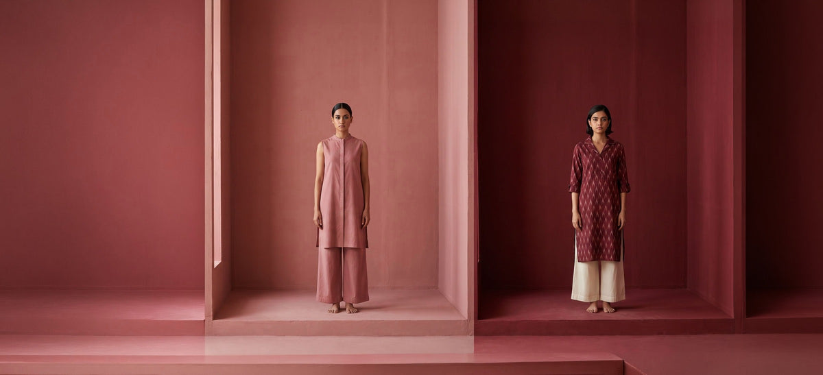 Two women in antique rose and maroon painted rooms, one in a rose tunic co-ord, one in a maroon kurta with an ikat collar