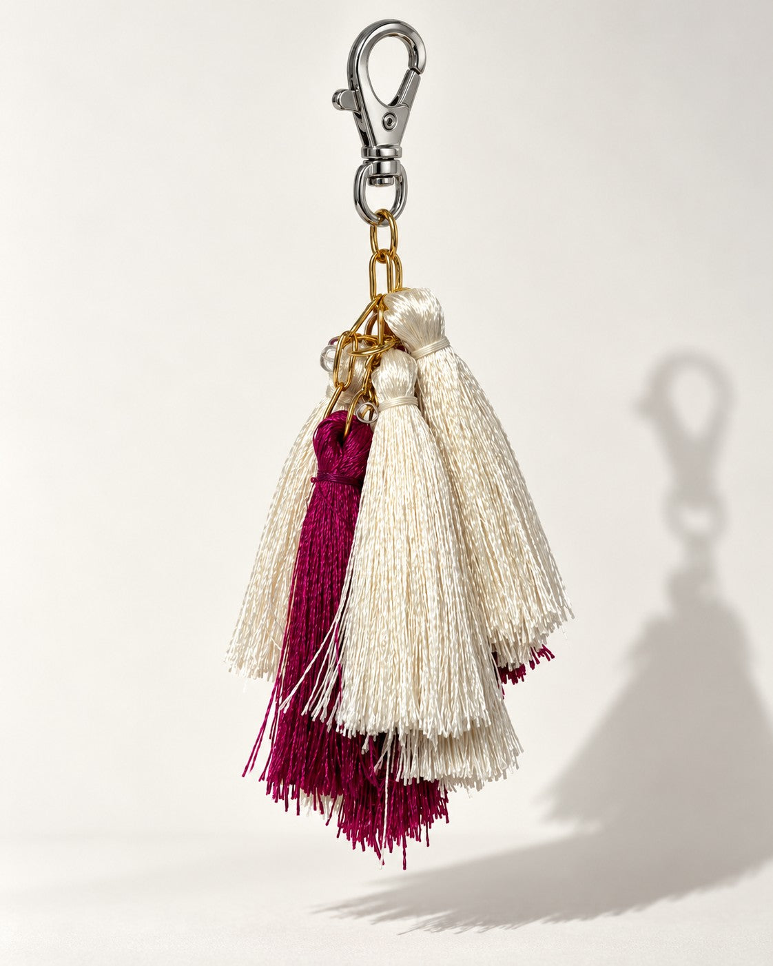 Gulal silk tassel bag charm: ivory silk tassels in front and magenta tassels behind them, hung from gold-tone chain links. It hangs from a silver-tone swivel clasp.