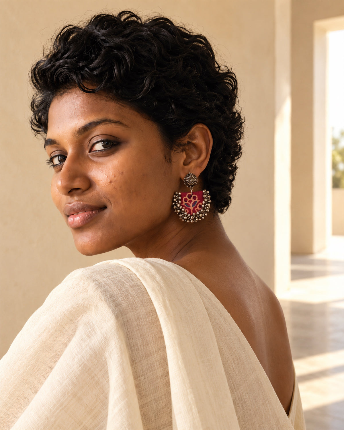 Maroon Chandbali Earrings with Ghungroo worn with short curls and a cream handloom drape in a sunlit colonnade: red block-printed fabric crescent with silver ghungroo bells