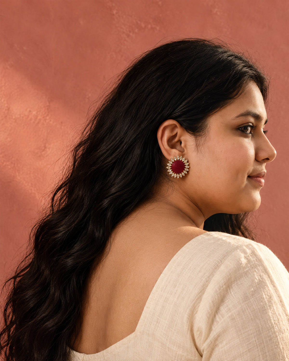 Maroon Floral Kundan Earrings, worn in profile, white top, terracotta pink wall