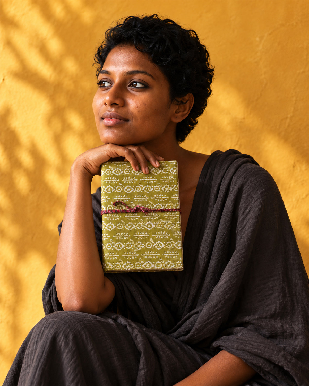 Mehendi Buti Block Print Fabric Diary, 200 Unruled Pages, held at the chin, black outfit, saffron yellow wall