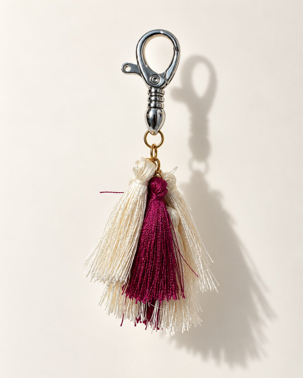Abeer silk tassel bag charm: ivory silk tassels with a single berry tassel set in front of them, on a gold-tone ring. It hangs from a silver-tone swivel clasp.