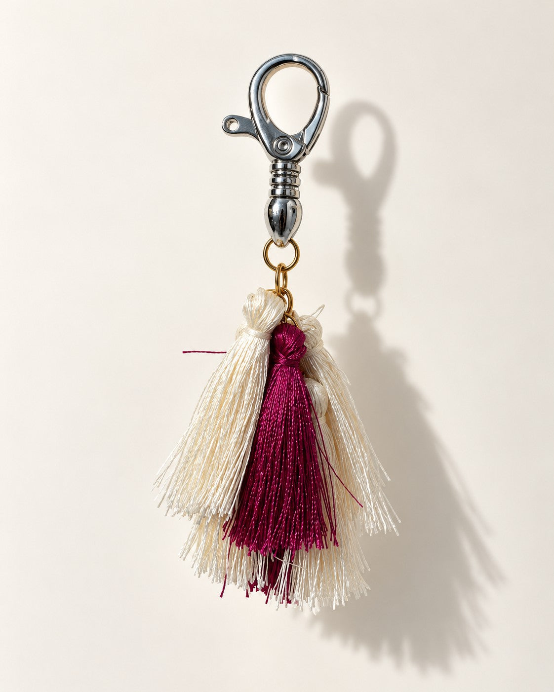 Abeer silk tassel bag charm: ivory silk tassels with a single berry tassel set in front of them, on a gold-tone ring. It hangs from a silver-tone swivel clasp.