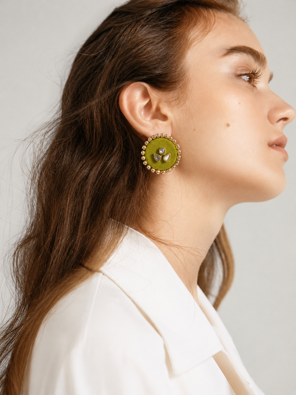 Lime green round kundan stud earring seen in profile with a white shirt: the Mogra stud, three kundan stones on lime green fabric ringed with small kundan
