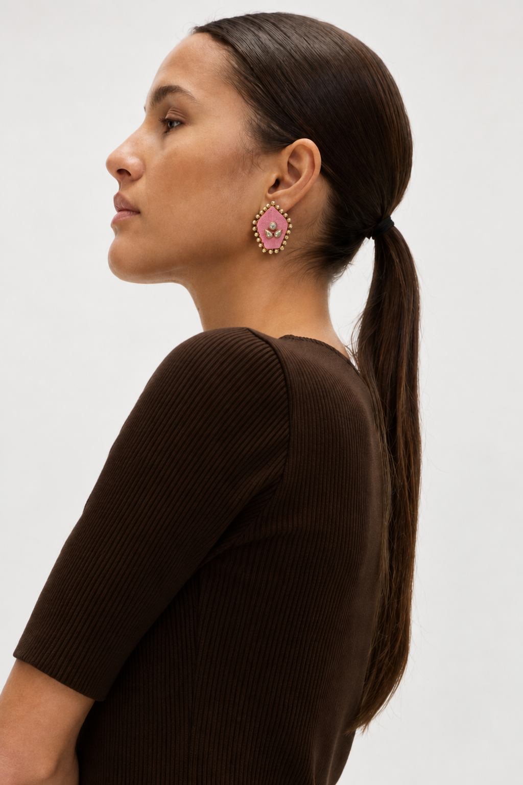 Mogra Pink Pentagon Kundan Stud in profile with a brown knit and a long ponytail: a soft pink five-sided fabric centre with three kundan stones and a small kundan border