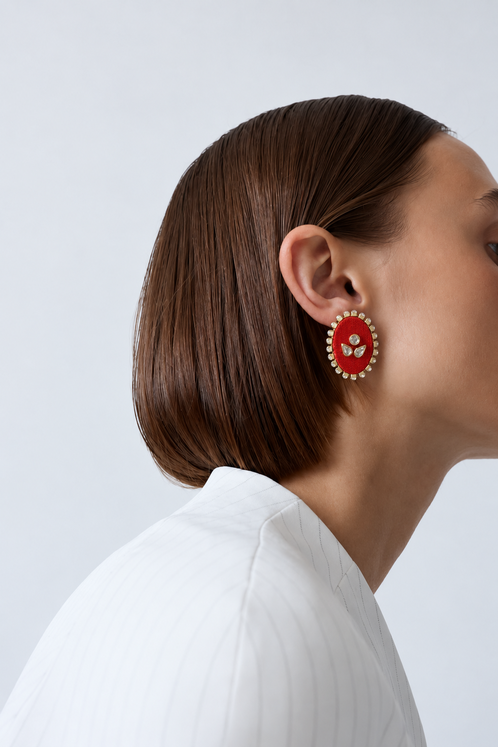 Red oval kundan stud earring in profile with a sleek bob and a white shirt