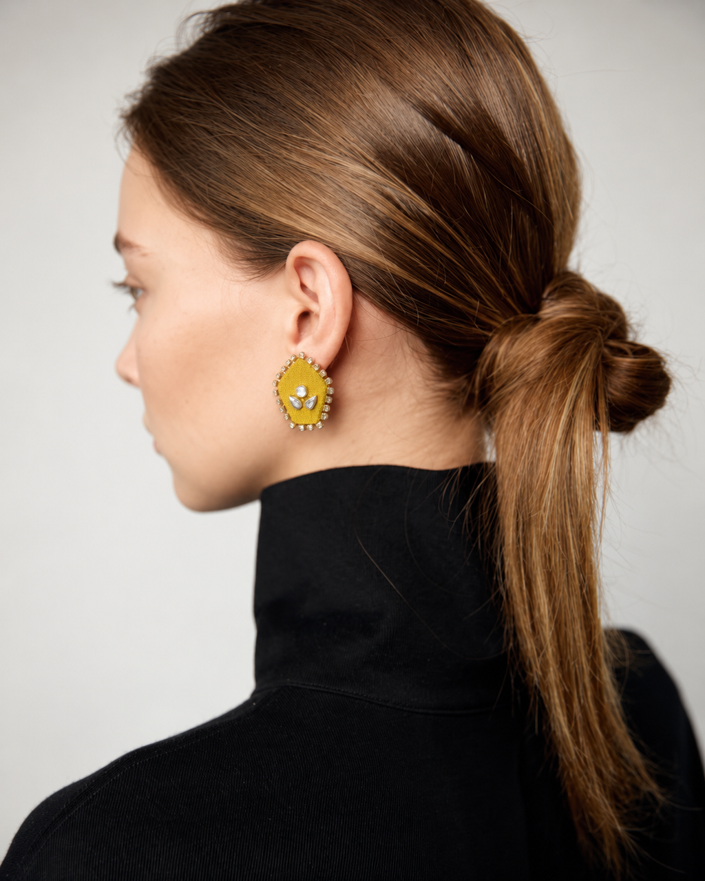Yellow pentagon kundan stud earring with a low ponytail and a black roll neck