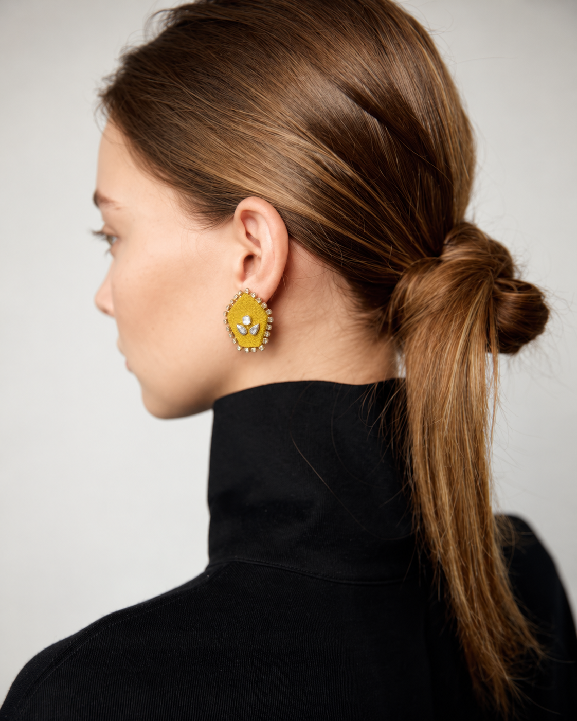 Yellow pentagon kundan stud earring with a low ponytail and a black roll neck