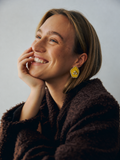 Mogra Yellow Pentagon Kundan Stud worn by a smiling model in a brown coat: a sunny yellow five-sided fabric centre with three kundan stones and a border of small kundan