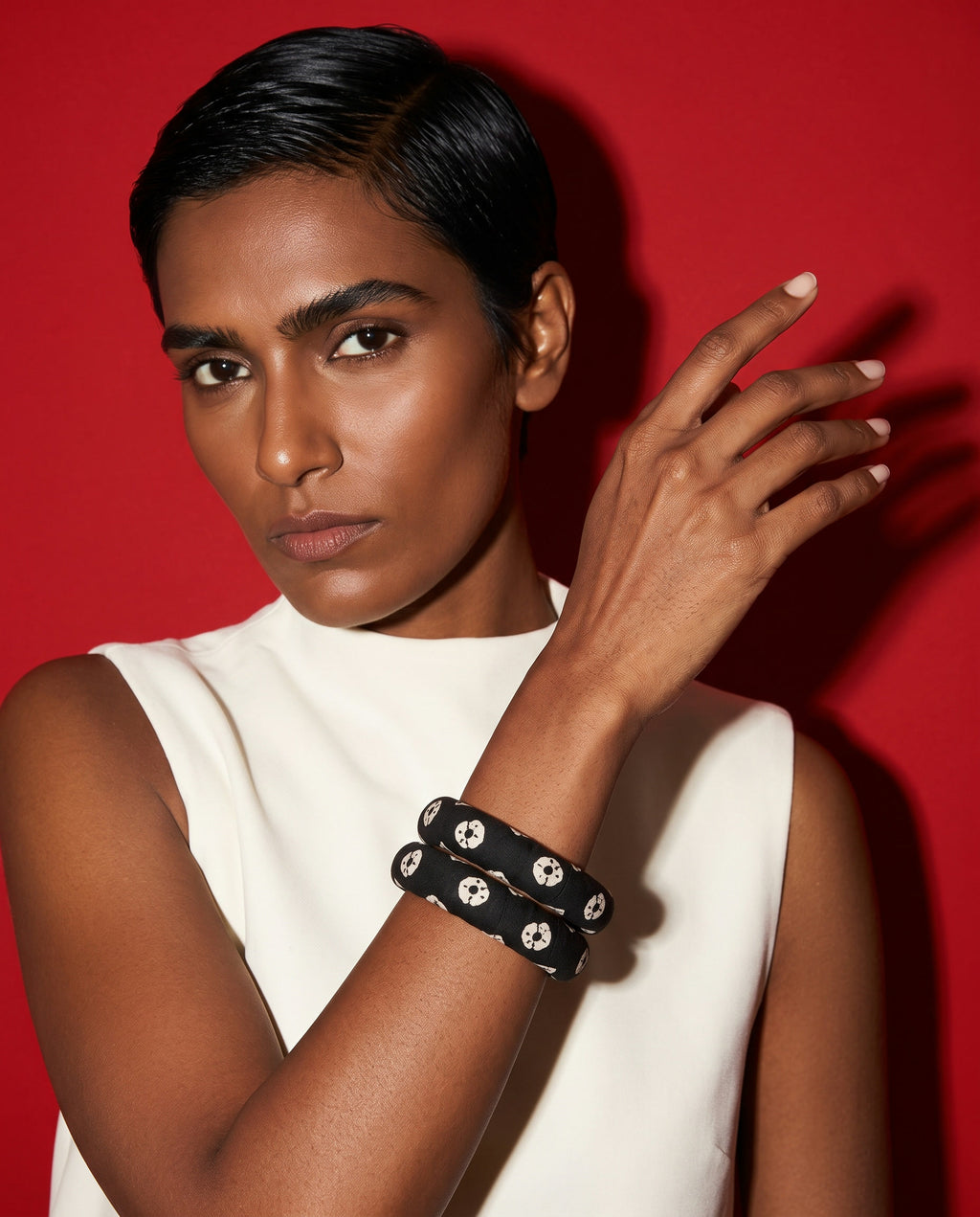 Black fabric bangles worn with a white top against a red backdrop
