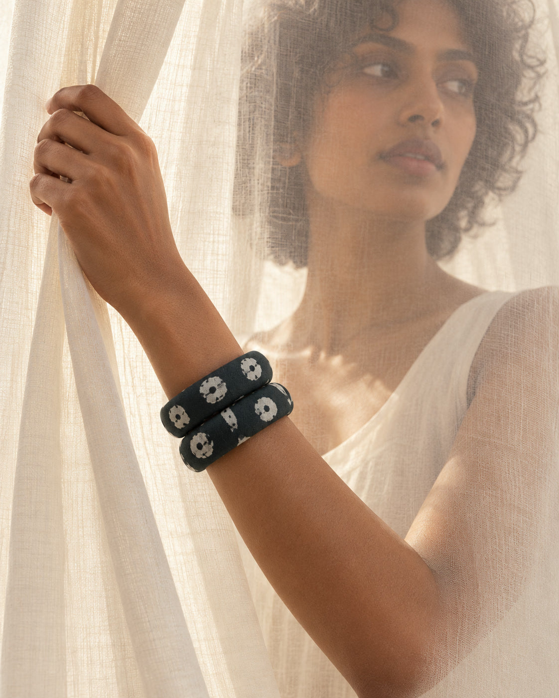Dark green printed fabric bangles worn beside a sheer curtain