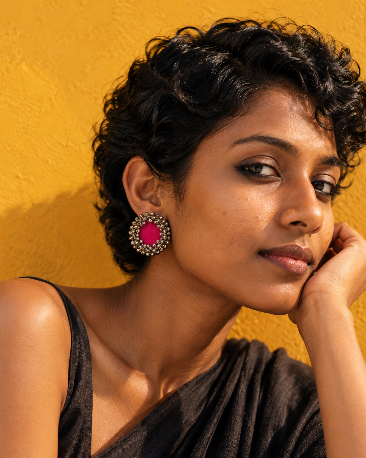 Fuchsia Pink Ghungroo Stud Earrings, worn, hand at the cheek, black top, saffron yellow wall