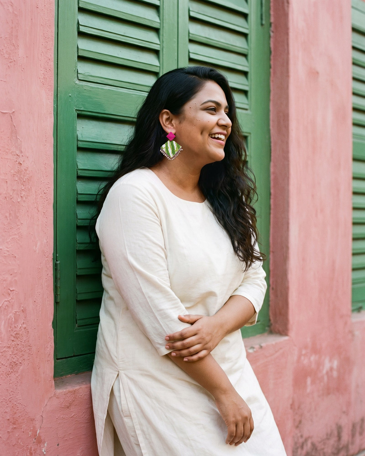 Fuchsia Pink Geometric Ghungroo Earrings worn with an ivory cotton kurta beside green wooden shutters (AI-generated styling image)