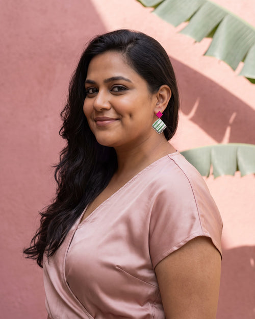 Fuchsia Pink Geometric Ghungroo Earrings worn with a blush satin top against a pink wall with banana-leaf shadows